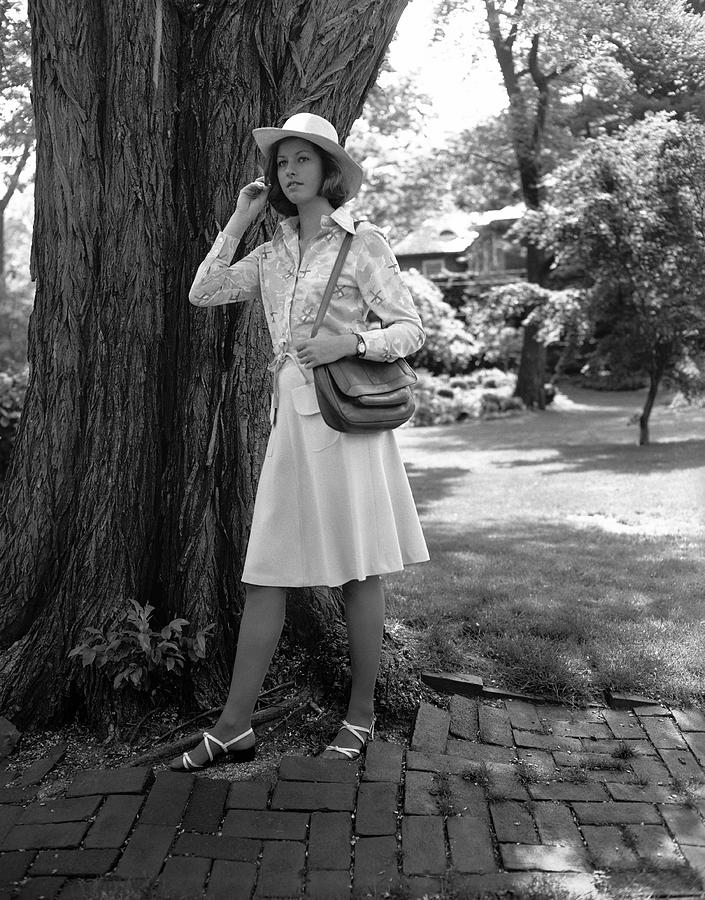 Young woman in hat standing by tree, (B&W), Photograph by George Marks