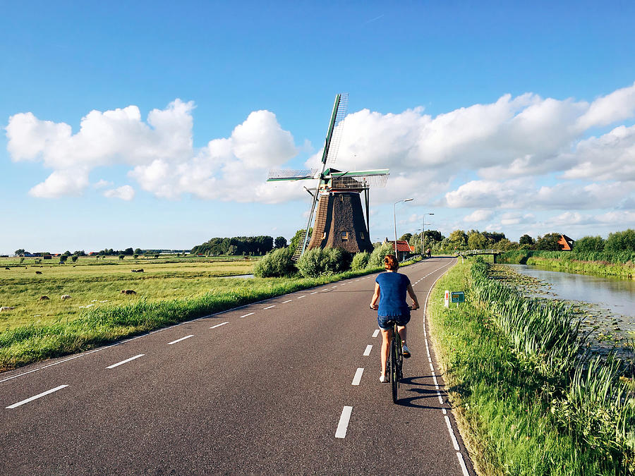 Young woman in shorts riding a bike near traditional Dutch windmill near Maasland, Holland, Netherlands Photograph by Alexander Spatari