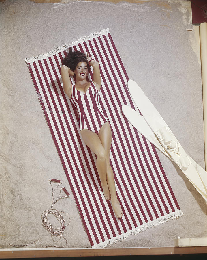 Young woman in striped swimwear lying on striped blanket, smiling, portrait Photograph by Tom Kelley Archive