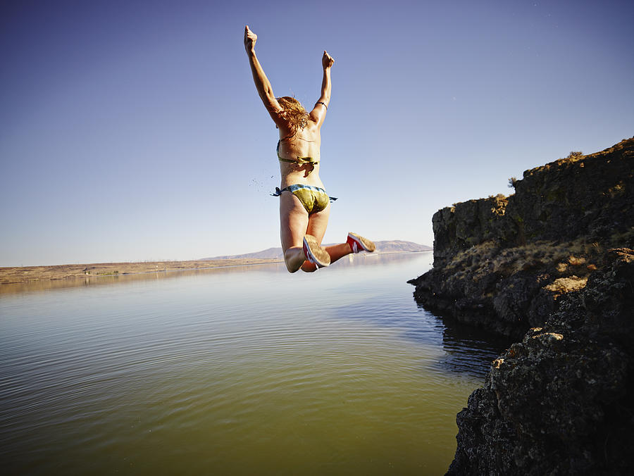 Young woman jumping off edge of cliff into river Photograph by Thomas Barwick