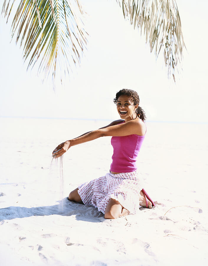 Young Woman Kneeling on a Beach With Sand Pouring From Her Hands Photograph by Digital Vision.