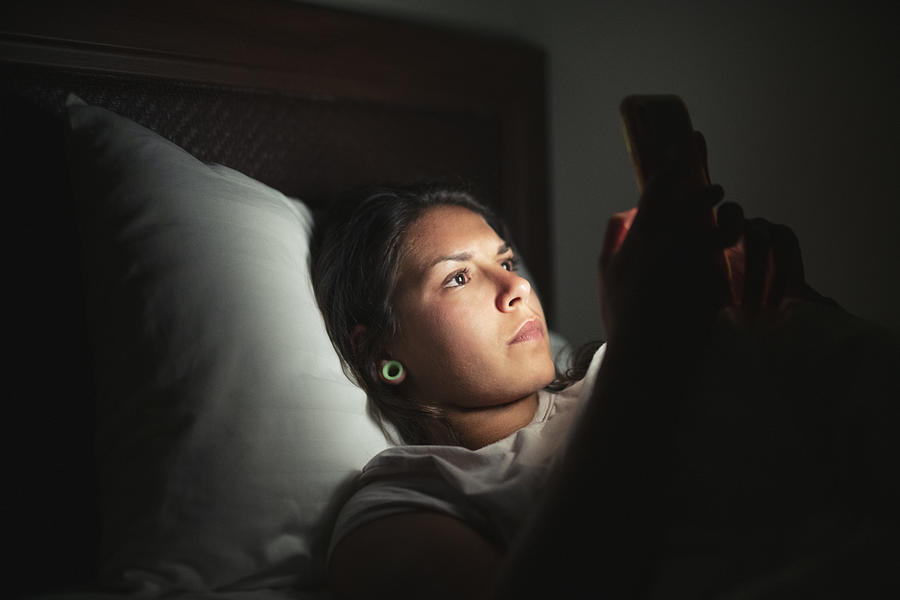 Young woman laying in bed and using smart phone. Photograph by ArtistGNDphotography