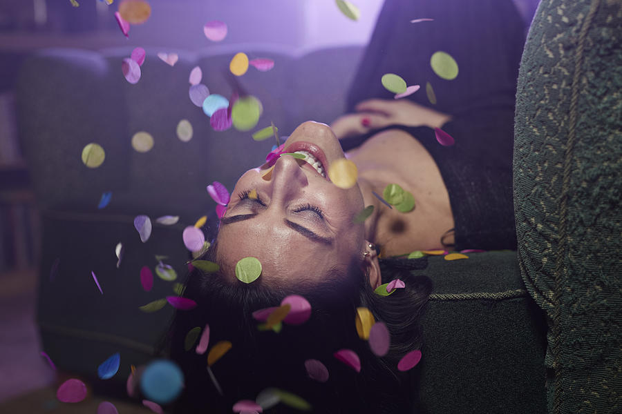 Young woman laying on sofa with confetti falling Photograph by Klaus Vedfelt