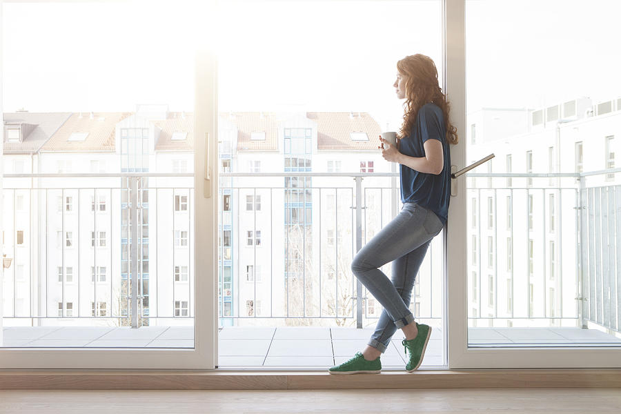 Young woman leaning at sliding door of balcony looking at distance Photograph by Westend61