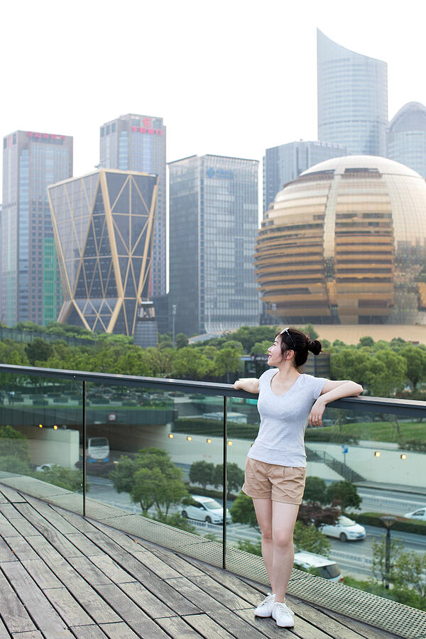 Young woman leaning on railing against urban skyline Photograph by Xia Yuan
