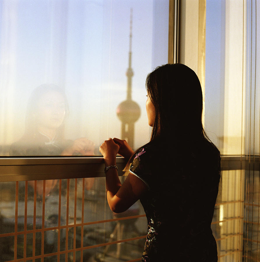 Young woman leaning on railing overlooking cityscape, dusk Photograph by Frank Rothe