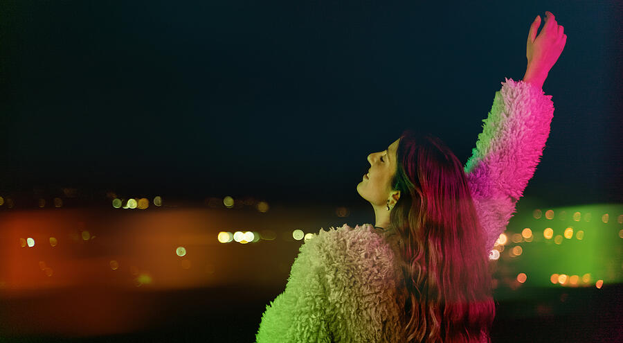 Young woman looking at city lights under colorful light Photograph by PepeLaguarda