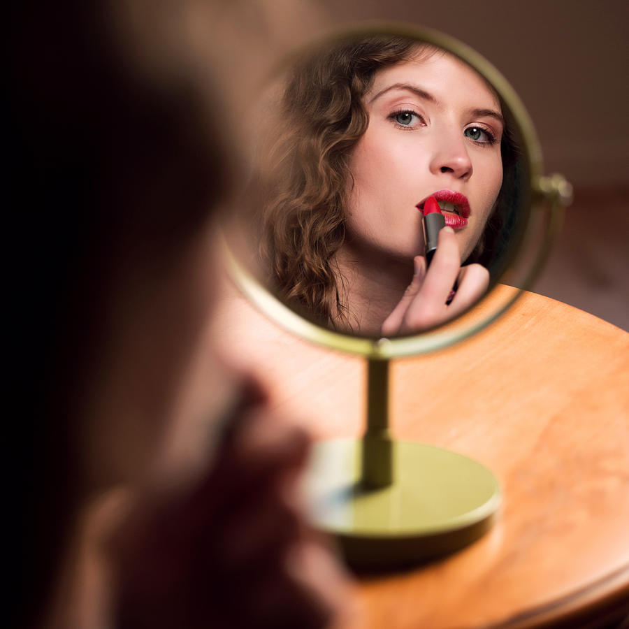 Young Woman Looking At Mirror Applying Lipstick Photograph by Stevecoleimages