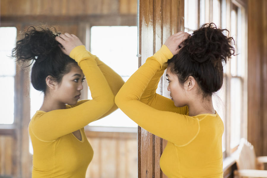 Young woman looking into mirror in rustic lodge Photograph by Tony Anderson