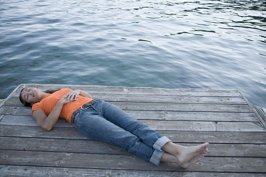 Young woman lying on dock, legs crossed at ankle, elevated view Photograph by Caroline Woodham