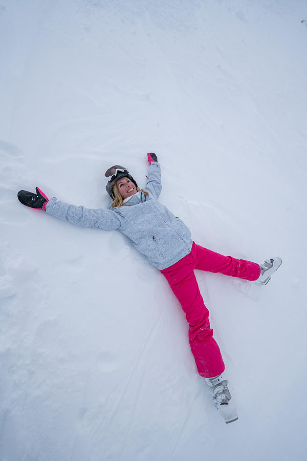 Young woman lying on snow playing snow angel Photograph by Swissmediavision