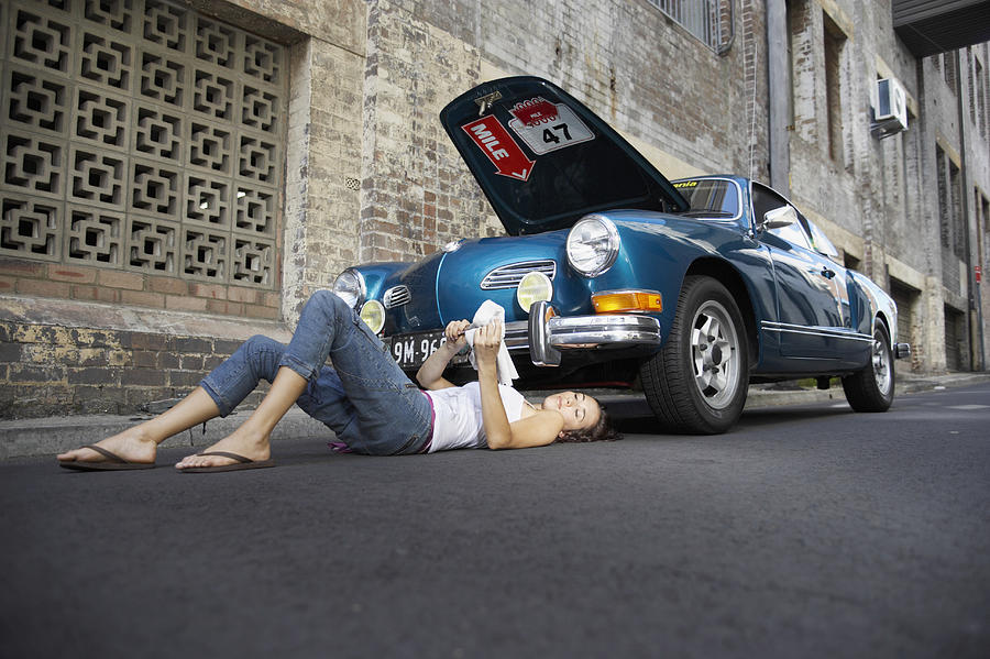 Young Woman Lying Underneath a Classic Car Cleaning a Tool Photograph by Digital Vision.