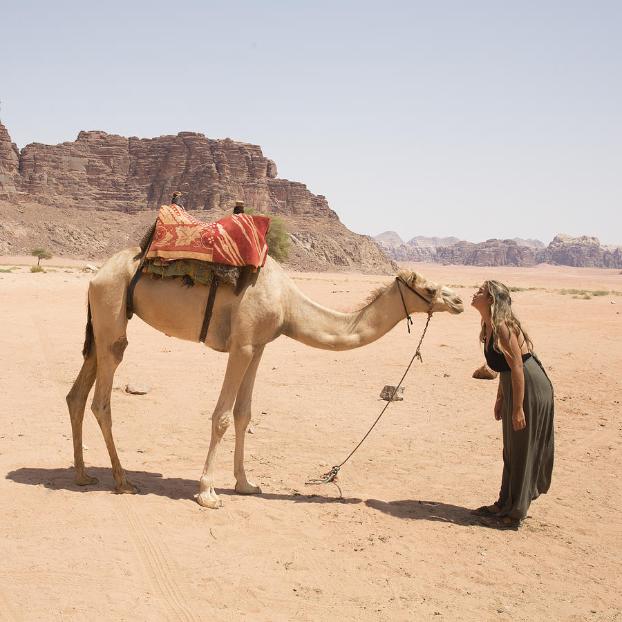 Young woman makes contact with camel in desert landscape Photograph by Ascent/PKS Media Inc.