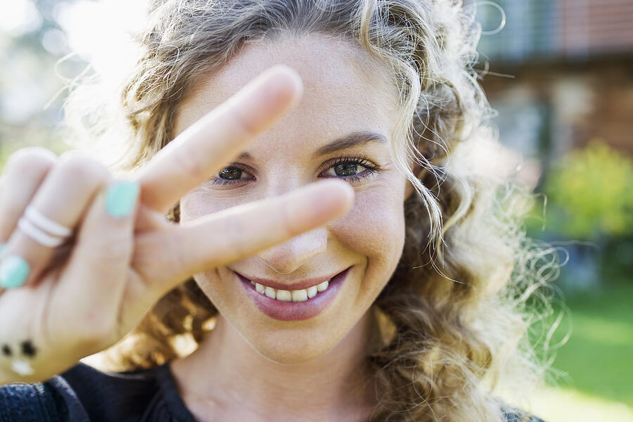 Young woman making peace sign with hand Photograph by Emely