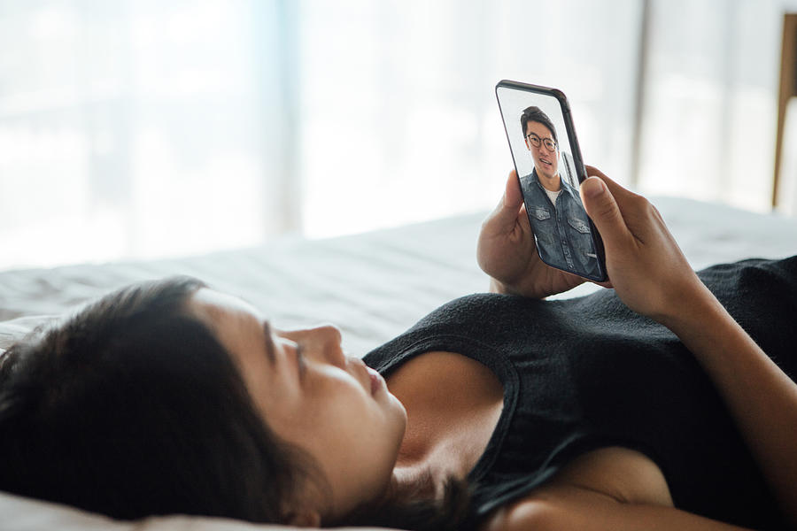 Young Woman Making Video Call With Smartphone In Bed Photograph by Oscar Wong