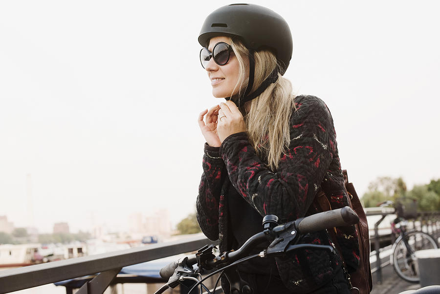 Young woman outdoors, putting on helmet, ready to ride bicycle Photograph by Max Bailen