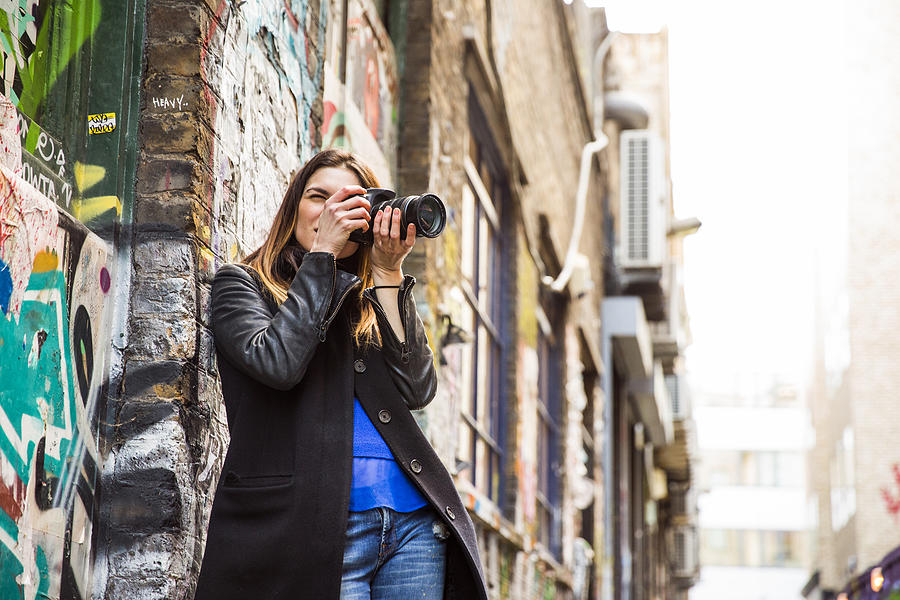 Young woman photographing in graffiti alley using DSLR Photograph by Tom Dunkley