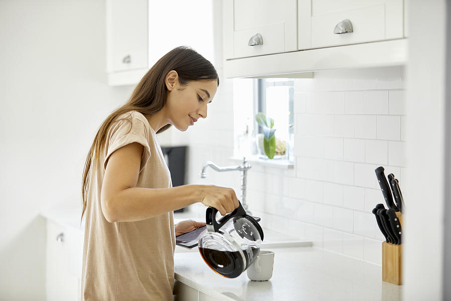 Young woman pouring coffee in cup at home Photograph by Morsa Images