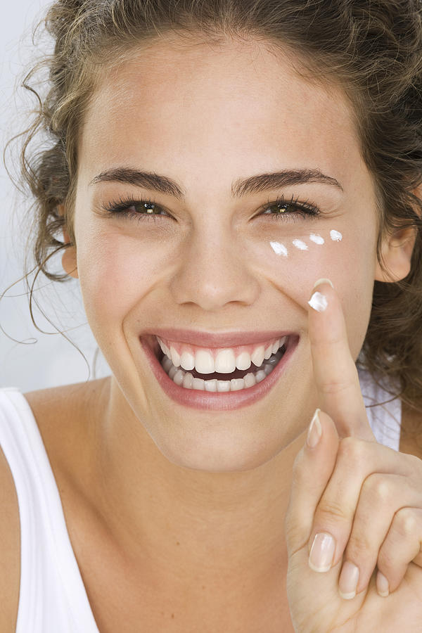 Young woman putting cream on face, smiling Photograph by Pando Hall