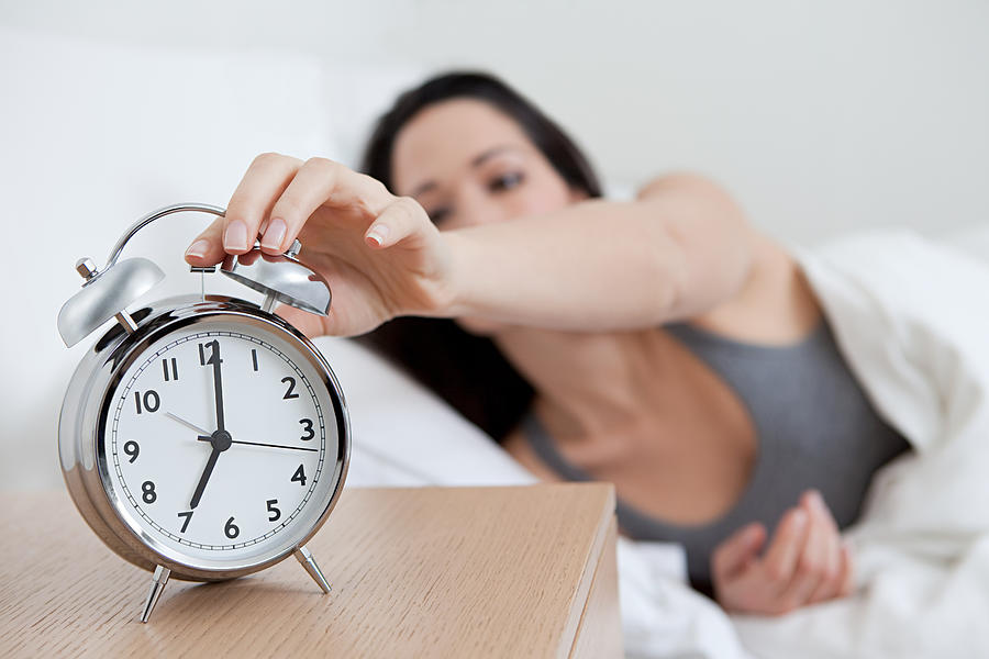 Young woman reaching for alarm clock Photograph by Image Source