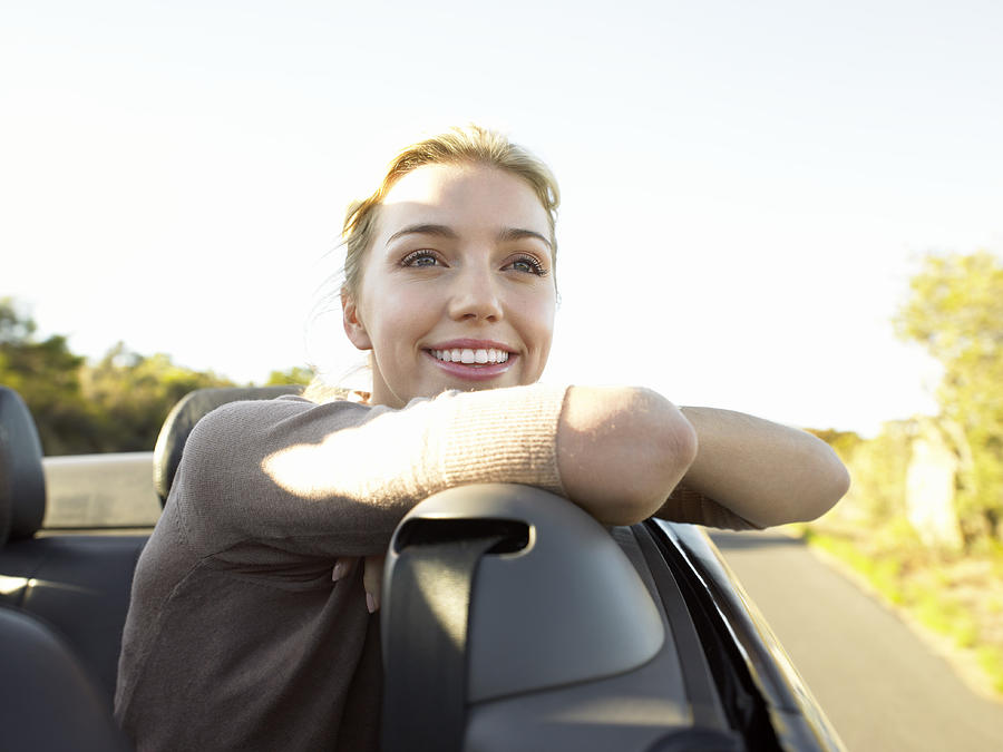 Young Woman Sits in the Back Seat of a Convertible Smiling at the View Photograph by Digital Vision.