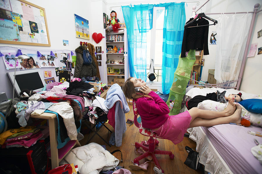 Young Woman Sits on a Chair in a Messy Bedroom Using a Mobile Phone Photograph by B2M Productions