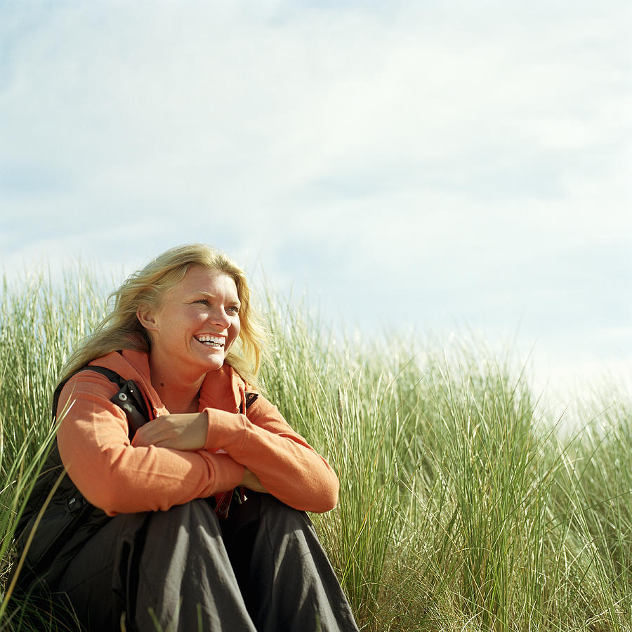 Young woman sitting amongst tall grass, smiling Photograph by Janie Airey