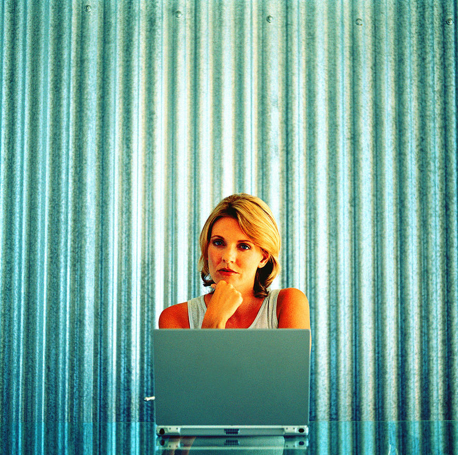 Young woman sitting and working on a laptop looking at camera Photograph by Stockbyte