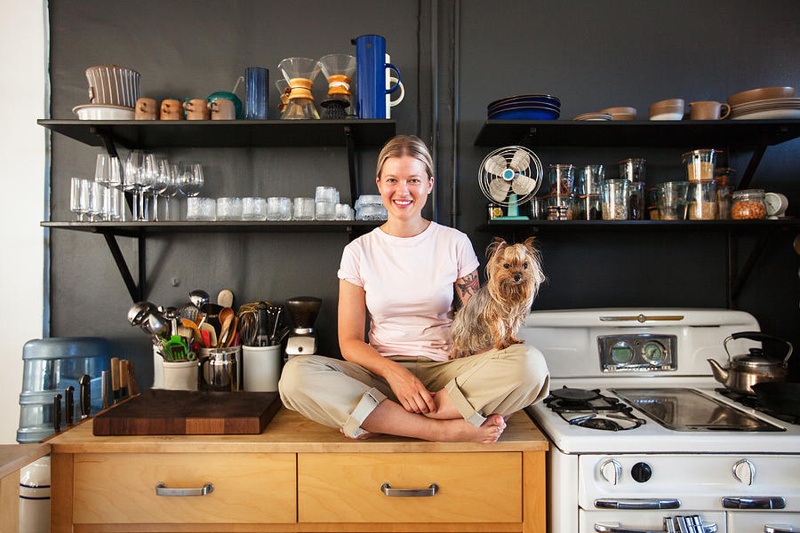 Young woman sitting in her kitchen with her dog Photograph by Stephen Zeigler