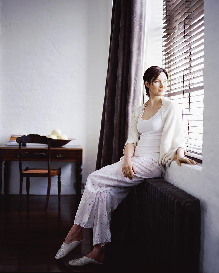 Young Woman Sitting on a Radiator Looking Out of a Window in a Home Showcase Interior Photograph by Digital Vision.