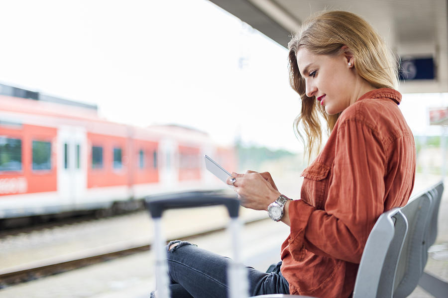Young woman sitting on bench at platform using tablet Photograph by Westend61