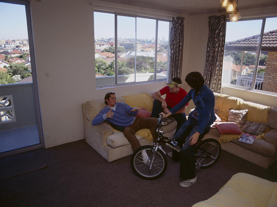 Young woman sitting on bike, while friends gather on sofa Photograph by Dex Image