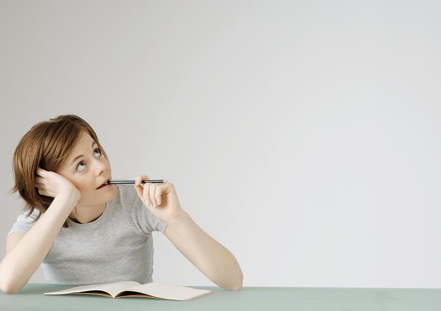 Young woman sitting with open notebook, holding pencil to mouth Photograph by Matthieu Spohn