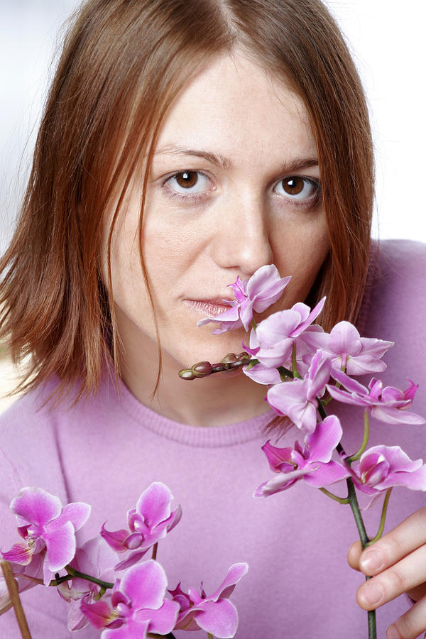 Young woman smelling orchid, portrait, close up Photograph by Loop Delay