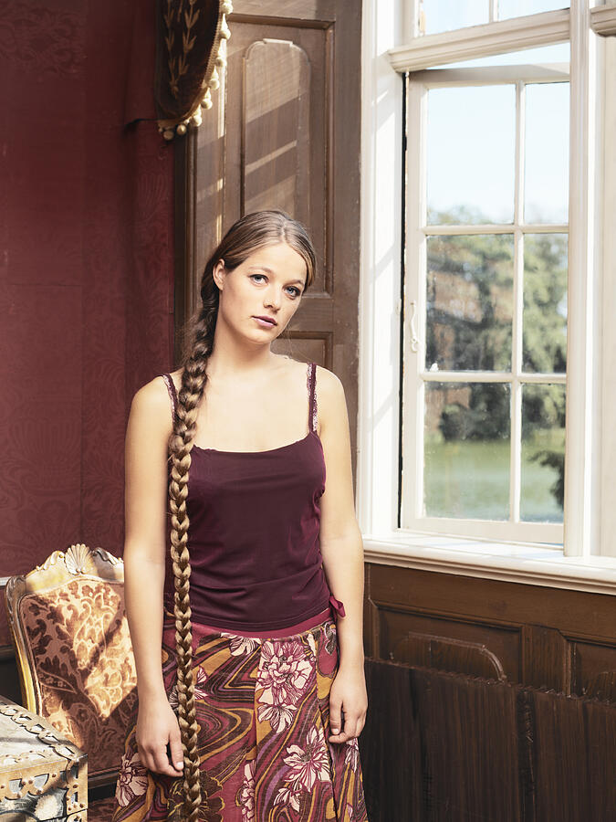 Young woman standing by bay window, portrait Photograph by Henrik Sorensen