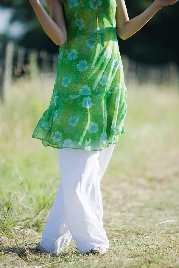 Young woman standing in rural field with legs crossed at knees, cropped view Photograph by ZenShui/Laurence Mouton