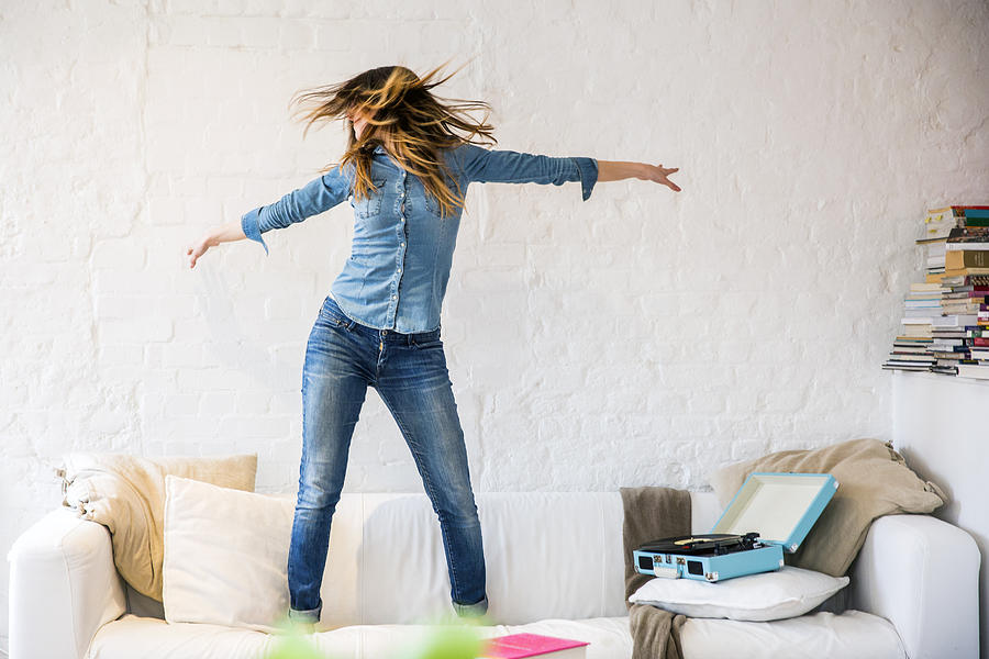 Young woman standing on sofa dancing and shaking her hair Photograph by Tom Dunkley