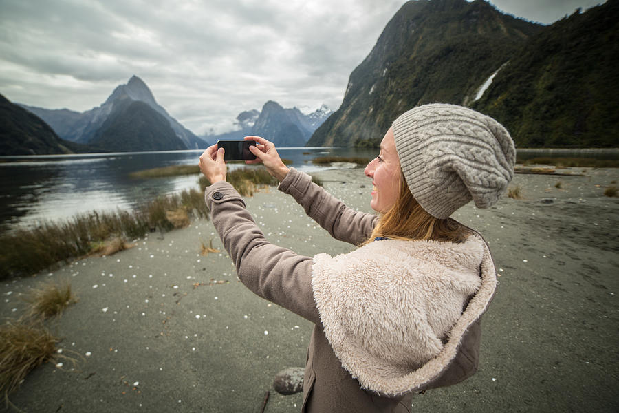 Young woman takes picture of mountain landscape with mobile phone Photograph by Swissmediavision