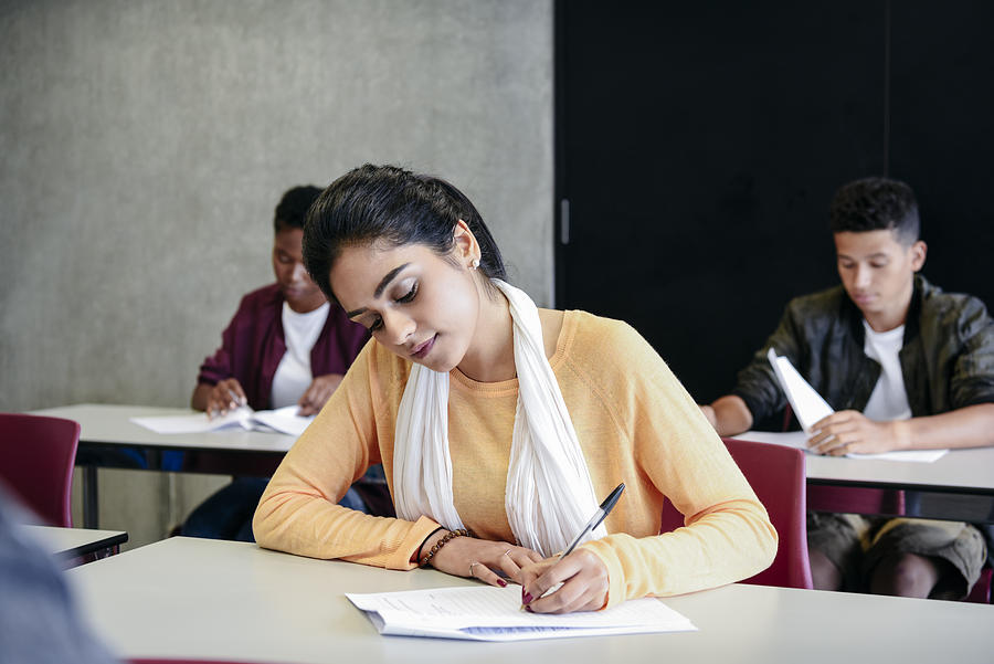 Young woman taking an exam writing at desk in classroom Photograph by JohnnyGreig