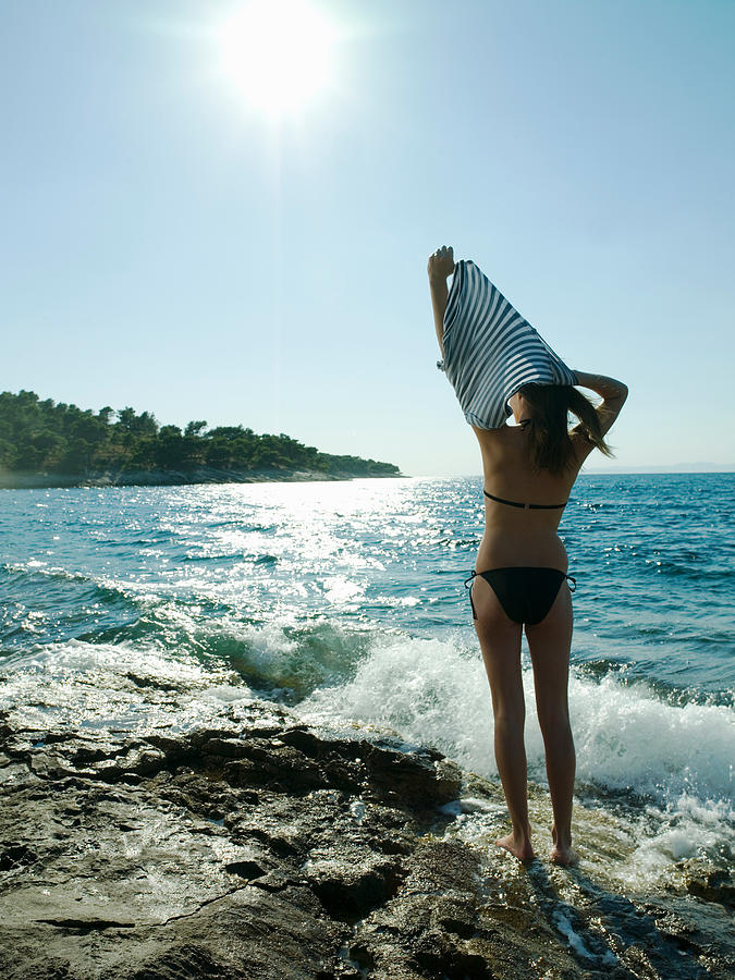 Young woman taking off t-shirt by the sea Photograph by Image Source