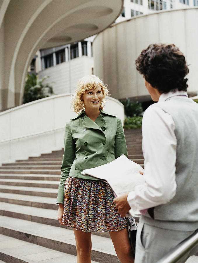 Young Woman Talking to a Man Standing on Steps by a Building in the City Photograph by Digital Vision.