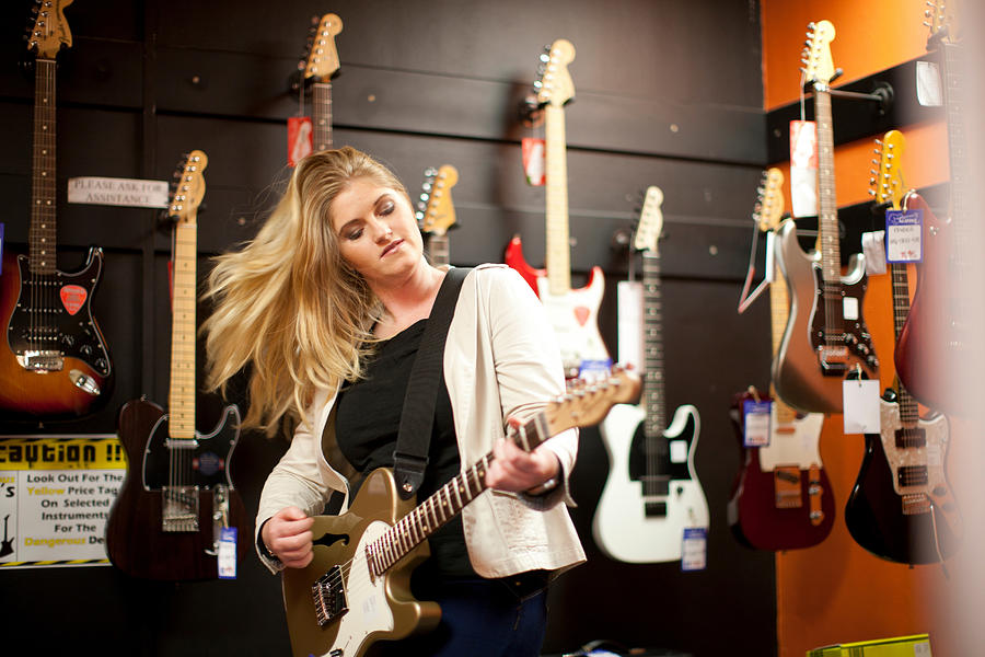 Young woman testing guitar in music store Photograph by Zero Creatives