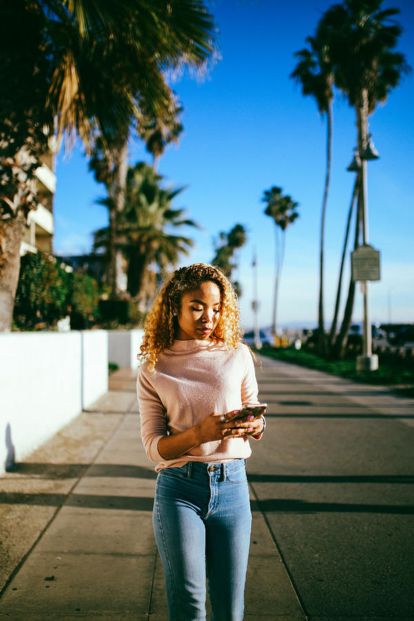 young woman texting on her cellphone on the Venice beach boardwalk in Los Angeles, California Photograph by Lechatnoir