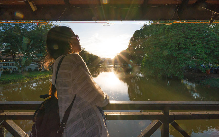 Young woman traverses bridge above tranquil river Photograph by Ascent/PKS Media Inc.