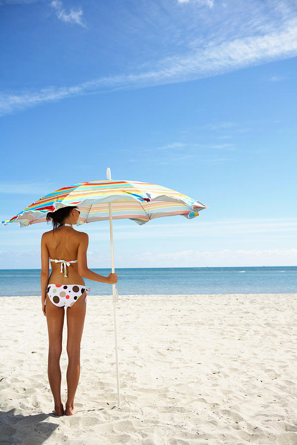 Young woman under beach umbrella, rear view Photograph by Kraig Scarbinsky