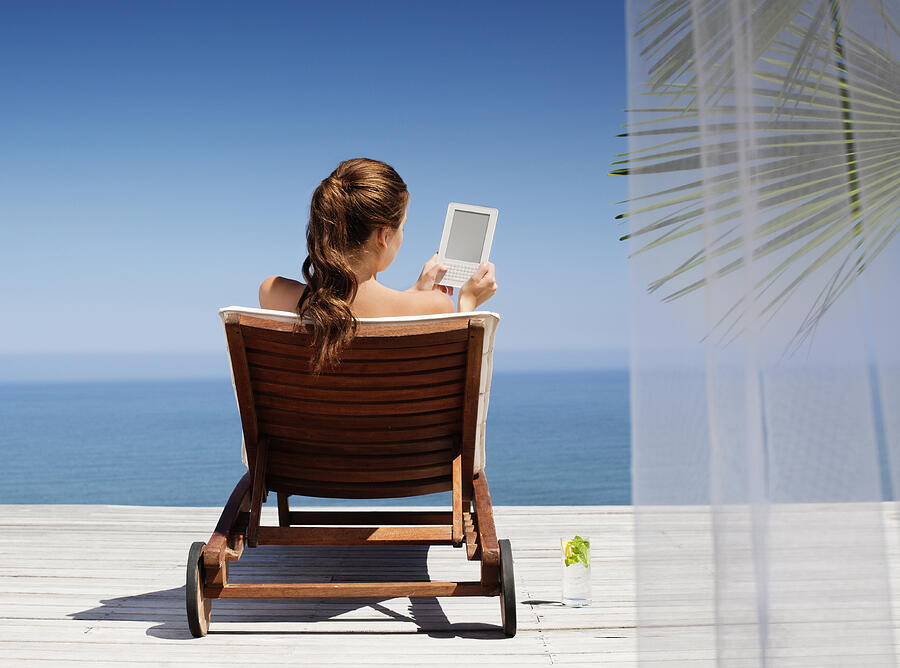 Young woman using an electronic reader while sitting on deck chair Photograph by OJO Images