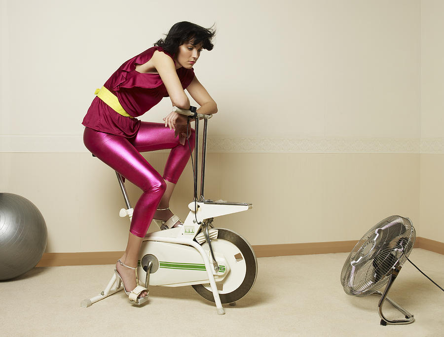Young woman using exercising bike Photograph by Jonathan Storey