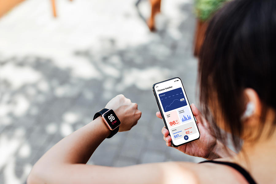 Young Woman Using Fitness Tracker App On Smart Watch And Smartphone Photograph by Oscar Wong