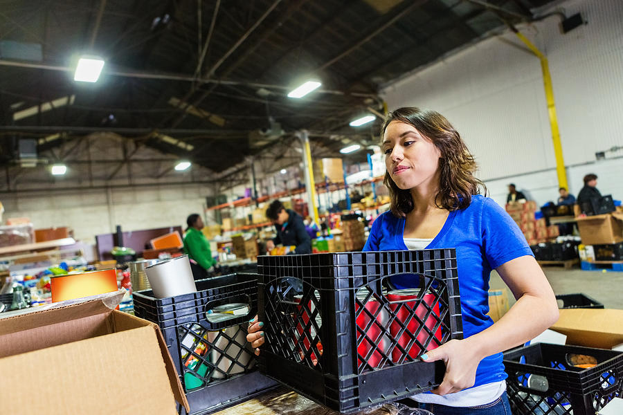 Young woman volunteering to organize donations in large food bank Photograph by SDI Productions