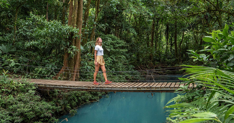 Young woman wandering in tropical rainforest walking on bridge over turquoise lagoon Photograph by Swissmediavision